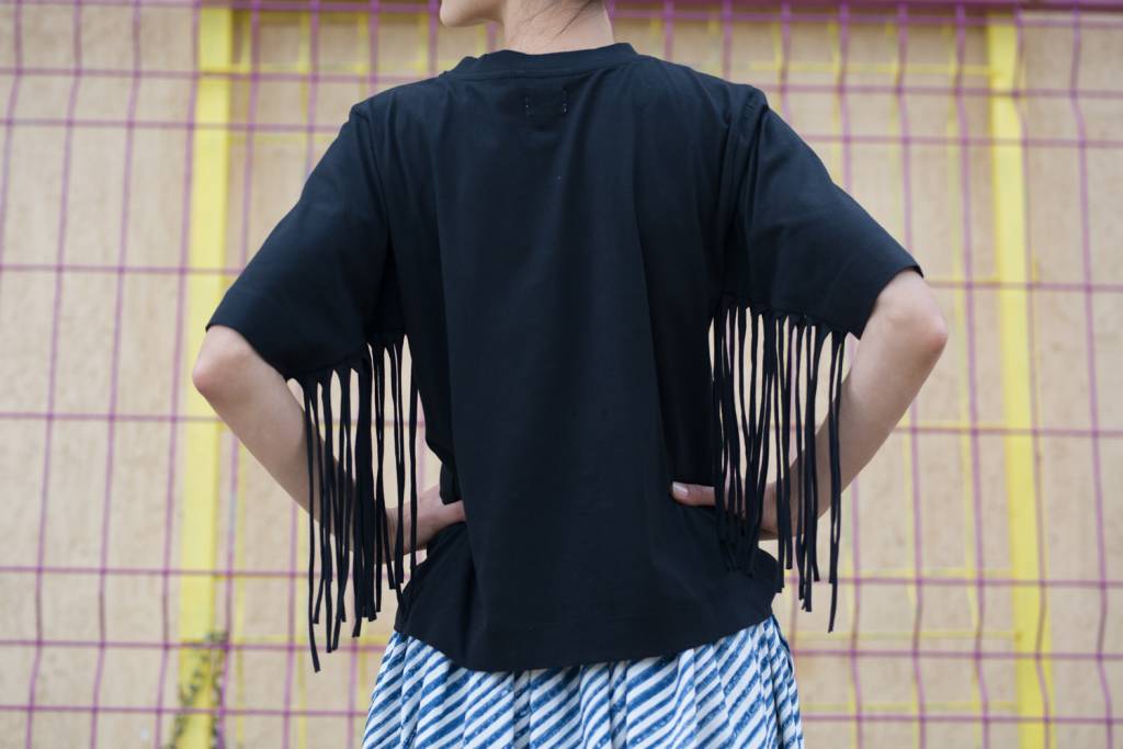 Organic cotton jersey tee with high round neck opening and long fringing detail at under-sleeve seam.